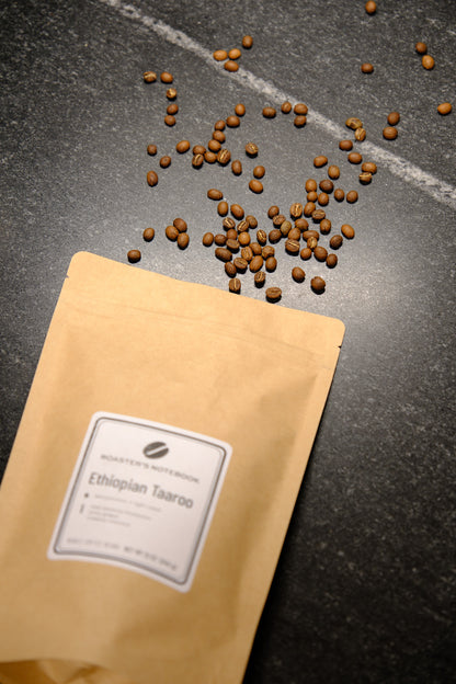 Coffee beans spilling out of a brown paper bag labeled 'Ethiopian Taaroo' on a dark surface.