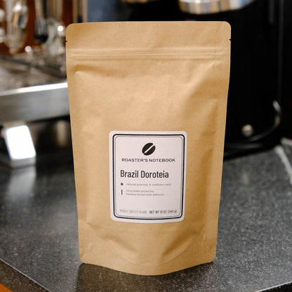 Coffee package labeled 'Brazil Dacoteia' on a counter with coffee-making equipment in the background