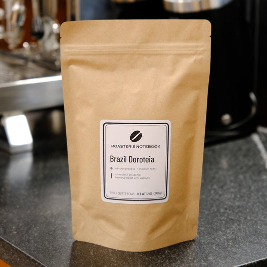 Coffee package labeled 'Brazil Dacoteia' on a counter with coffee-making equipment in the background